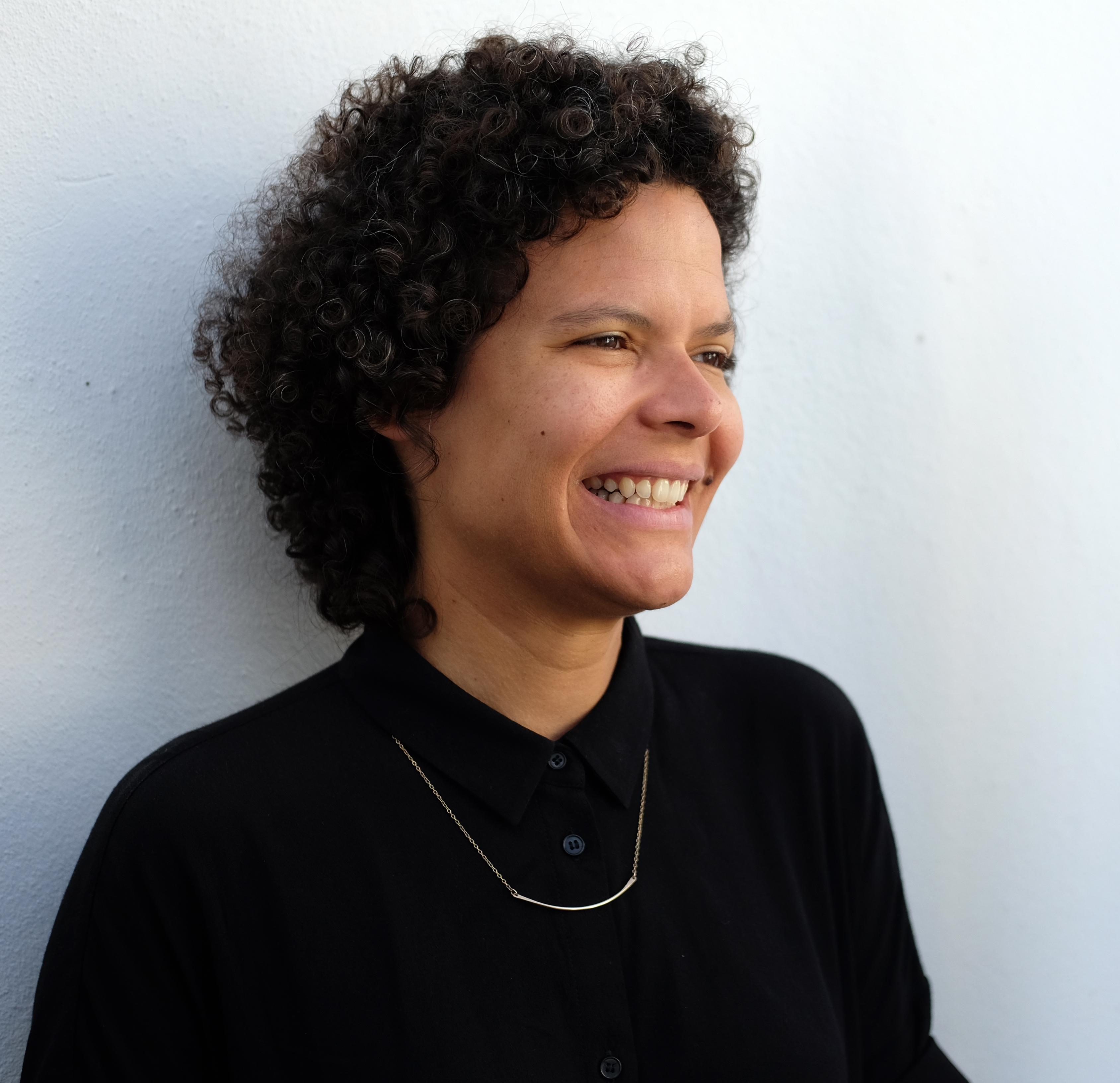 Patricia Benabe is wearing a black long sleeve, looking into the distance, smiling.