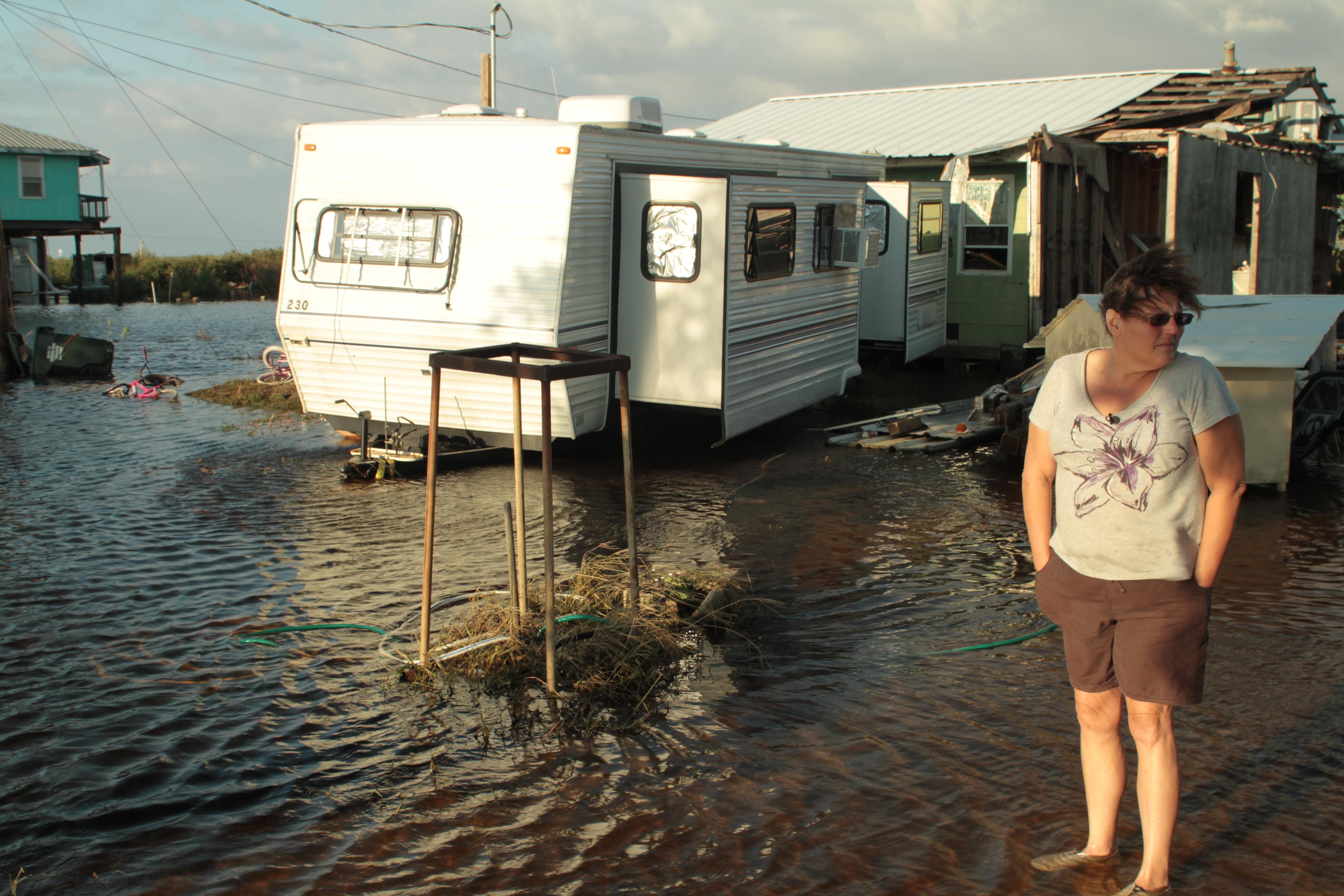 A person stands in a flooded area in front of a mobile home.