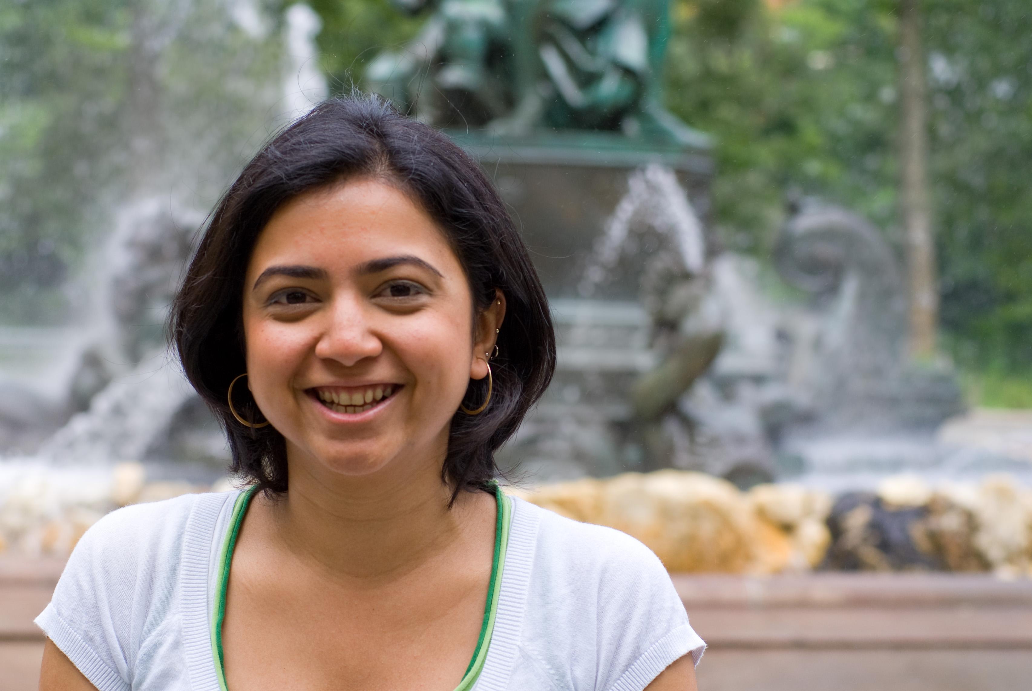 A photo of a woman in front of a fountain smiling at the camera.