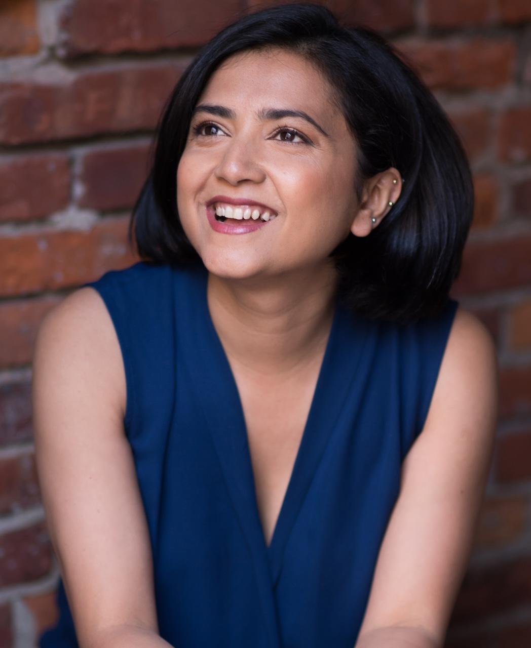 A photo of a woman smiling, looking off to the corner.