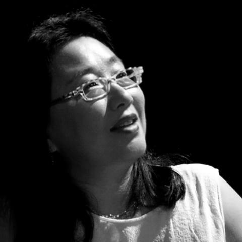 Renee Tajima-Pena looks away from the camera. She is wearing thin glasses and smiles slightly. The portrait is in black and white.