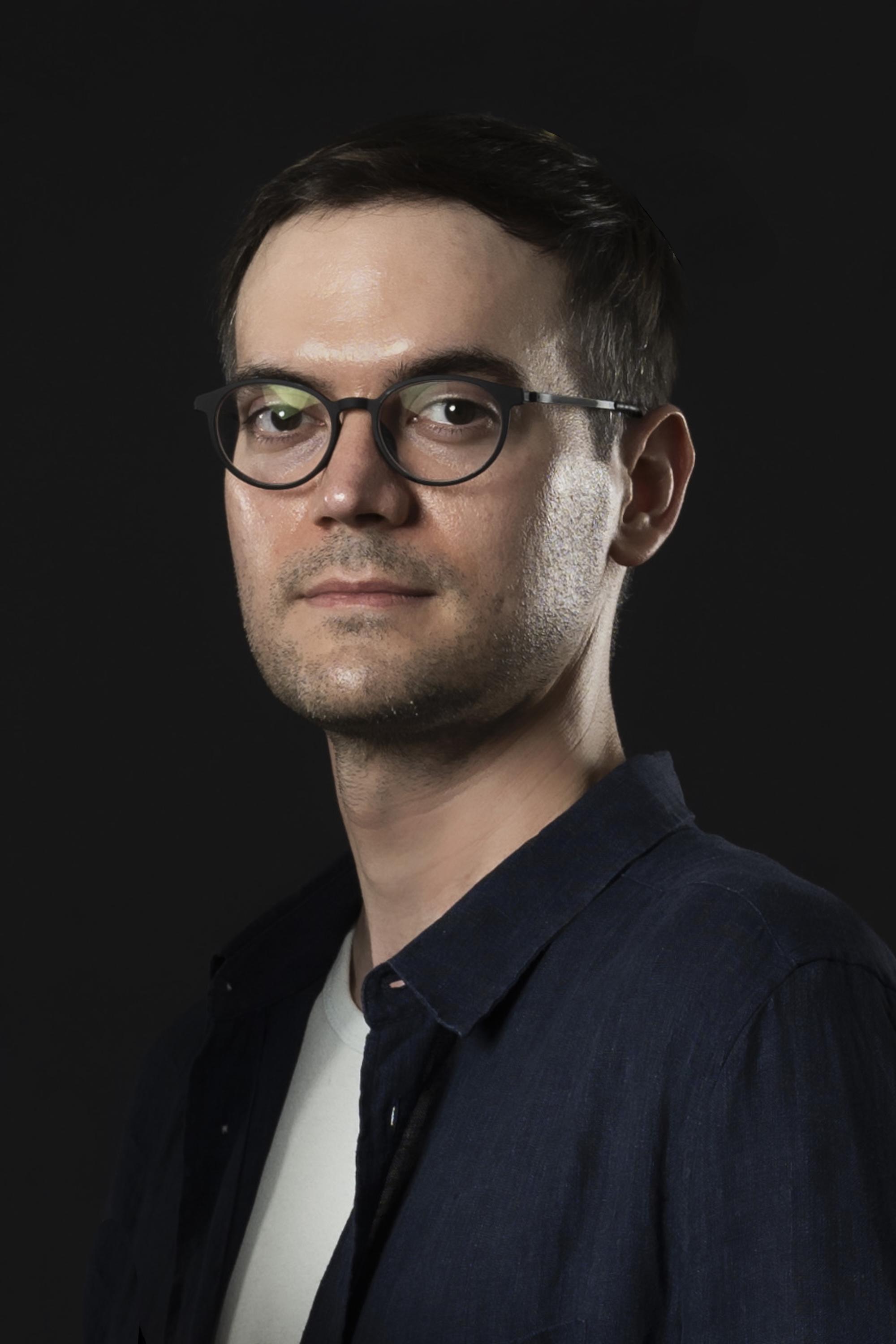 Portrait of a man wearing glasses and a neutral expression against a black background