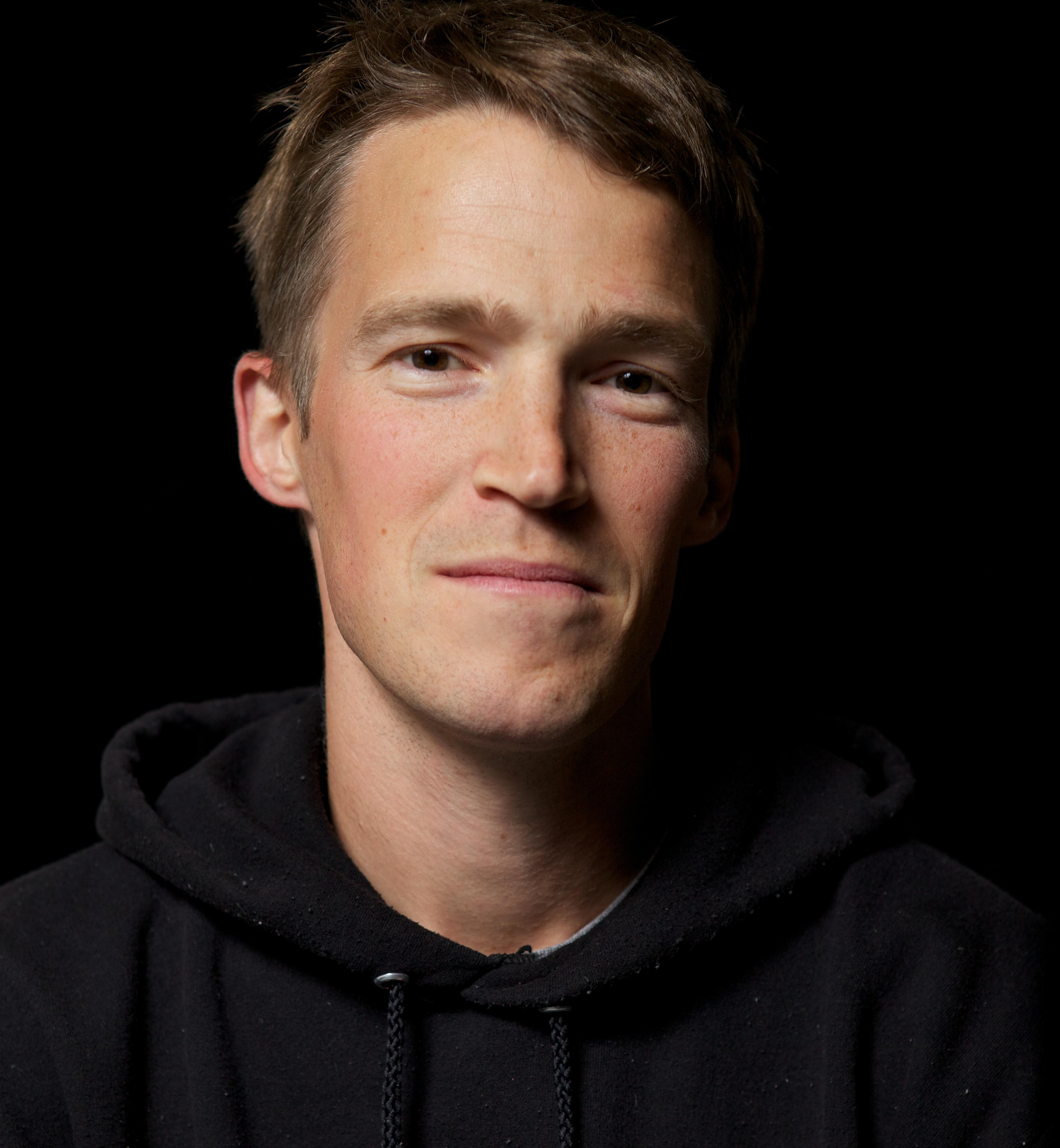 A portrait of a man looking into the camera in front of a black backdrop.