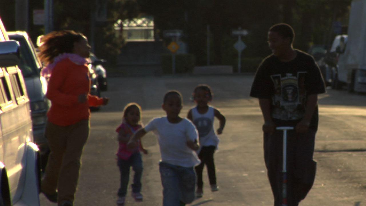 Two teenagers and three young children run down the street during golden hour.