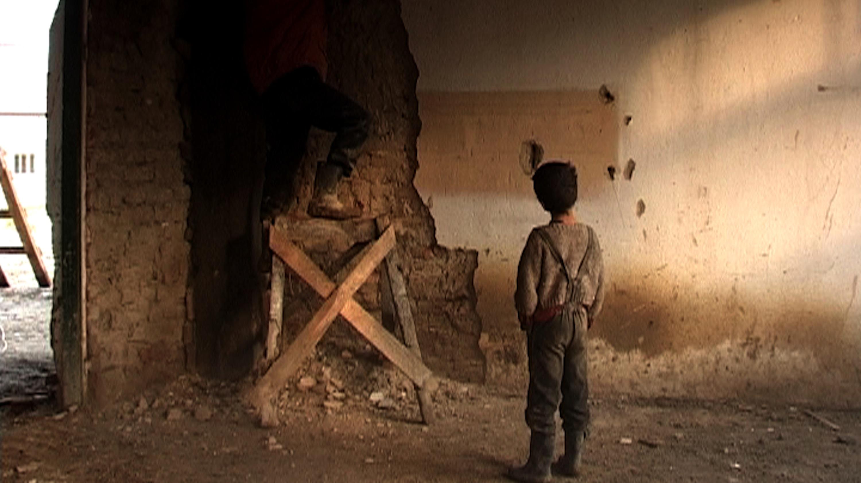 A young child stands in a dilpidated building and looks at what looks to have been a podium.