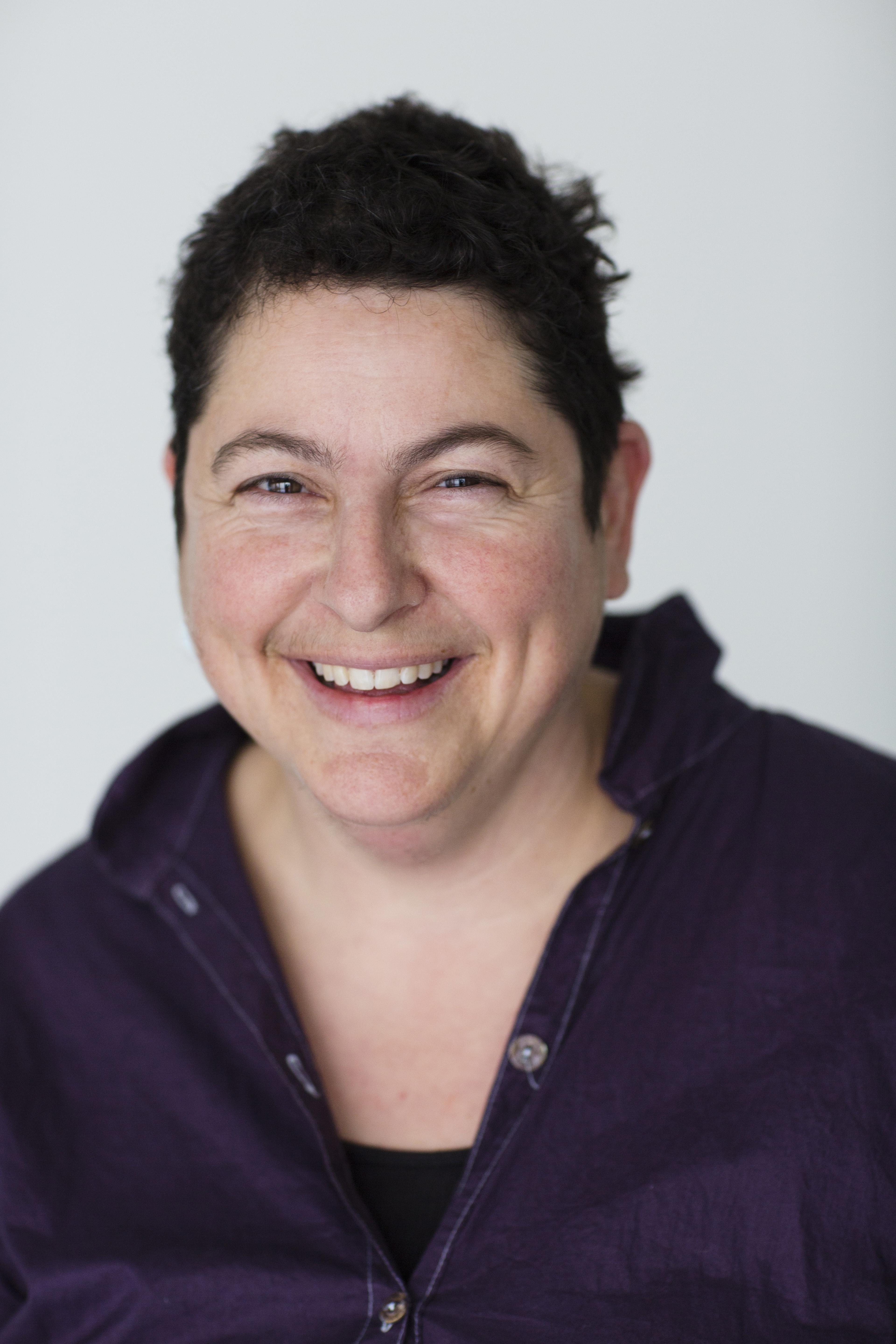 A photo of a woman laughing in front of a white backdrop.