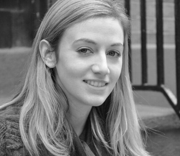 A black and white photo of a woman sitting on steps and smiling at the camera.