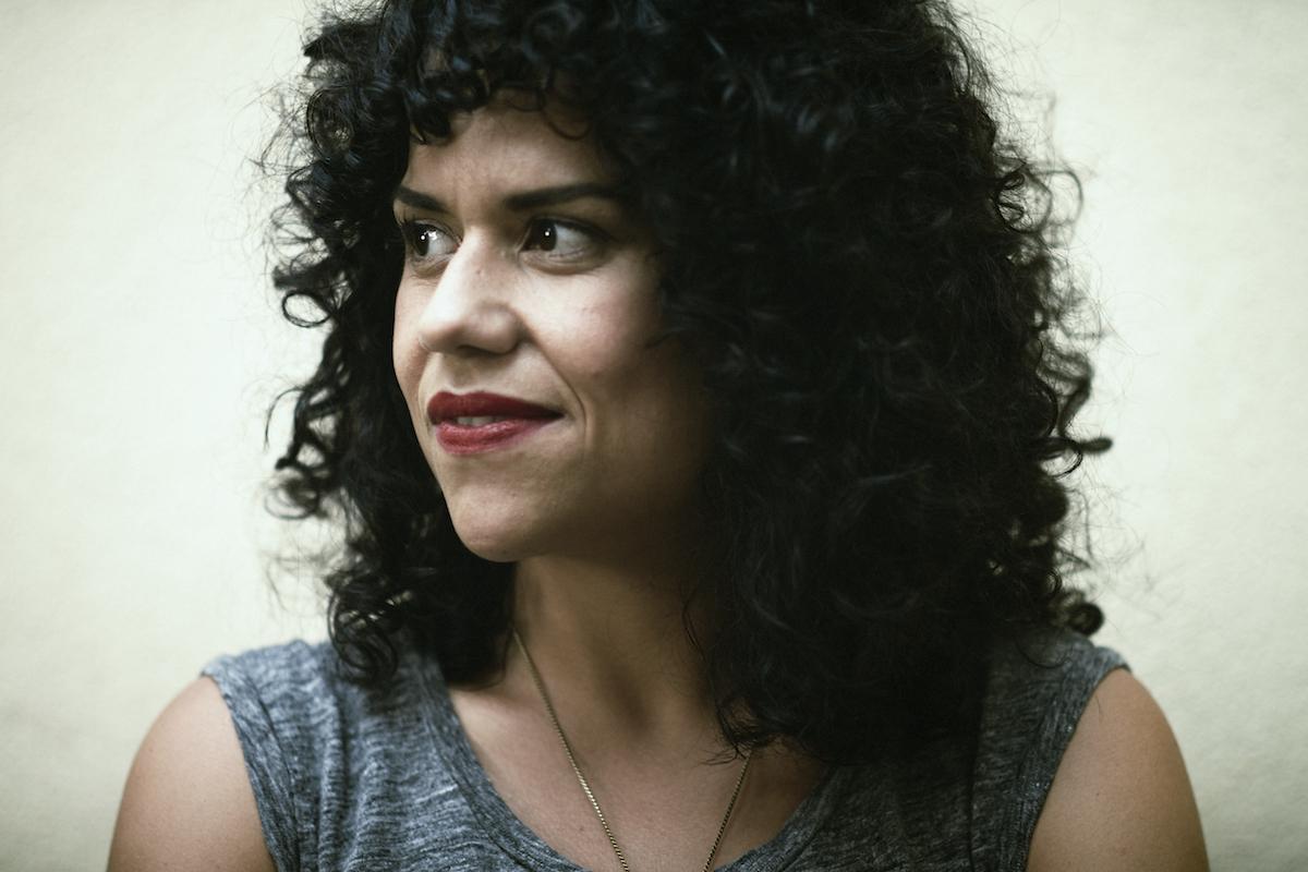 Cecilia Aldarondo is looking away from the camera. She has medium curly hair and is wearing lipstick.