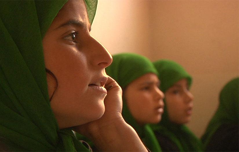 A group of young girls sit in the back of a classroom at school.