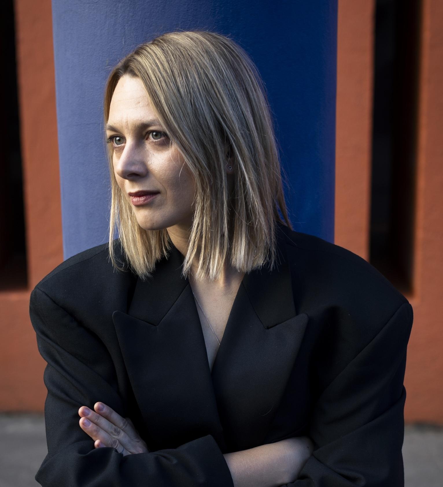 Oksana Karpovych looking to the side and wearing a black pantsuit.