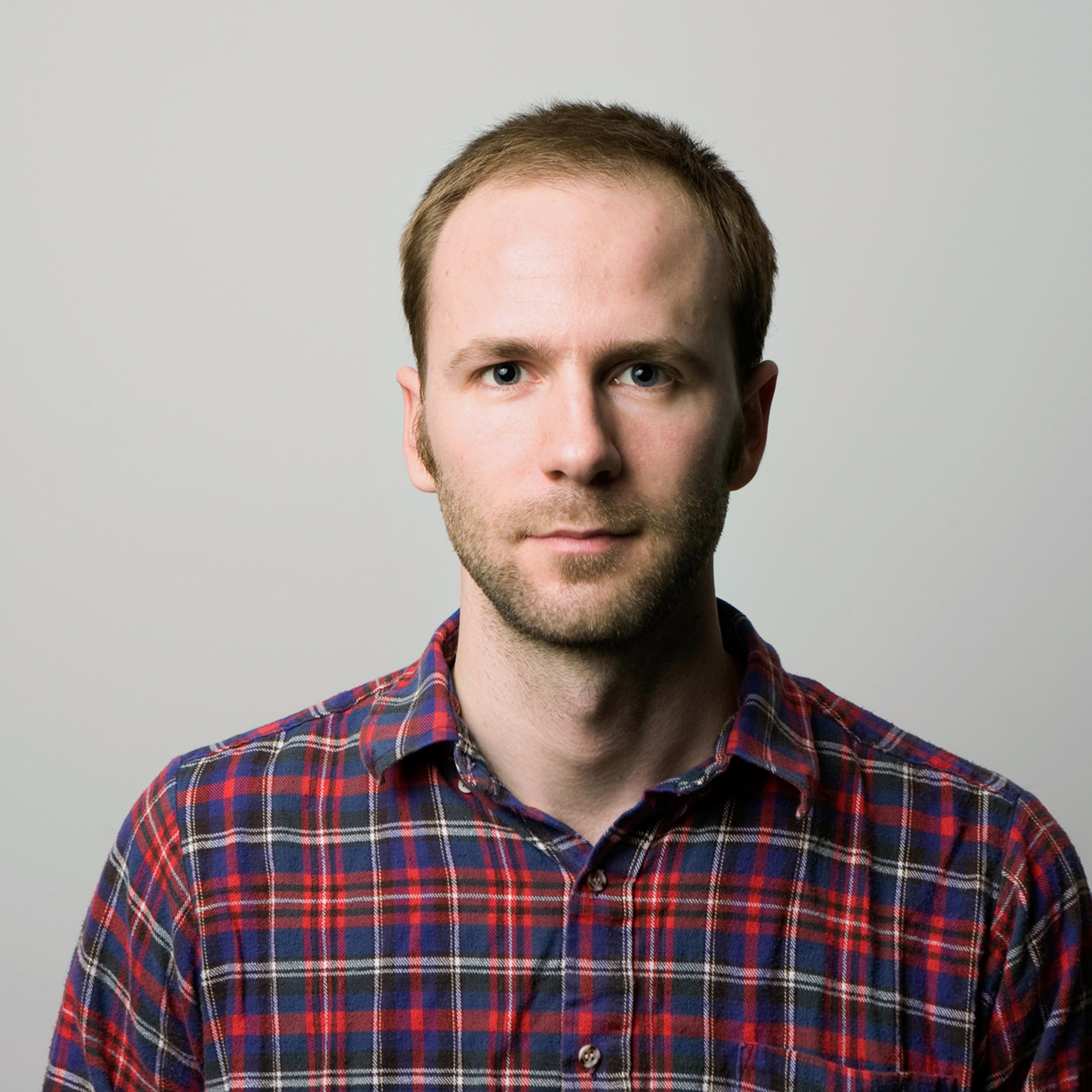 Robin Blotnick stares at the camera smiling. He has short hair and is wearing a plaid shirt