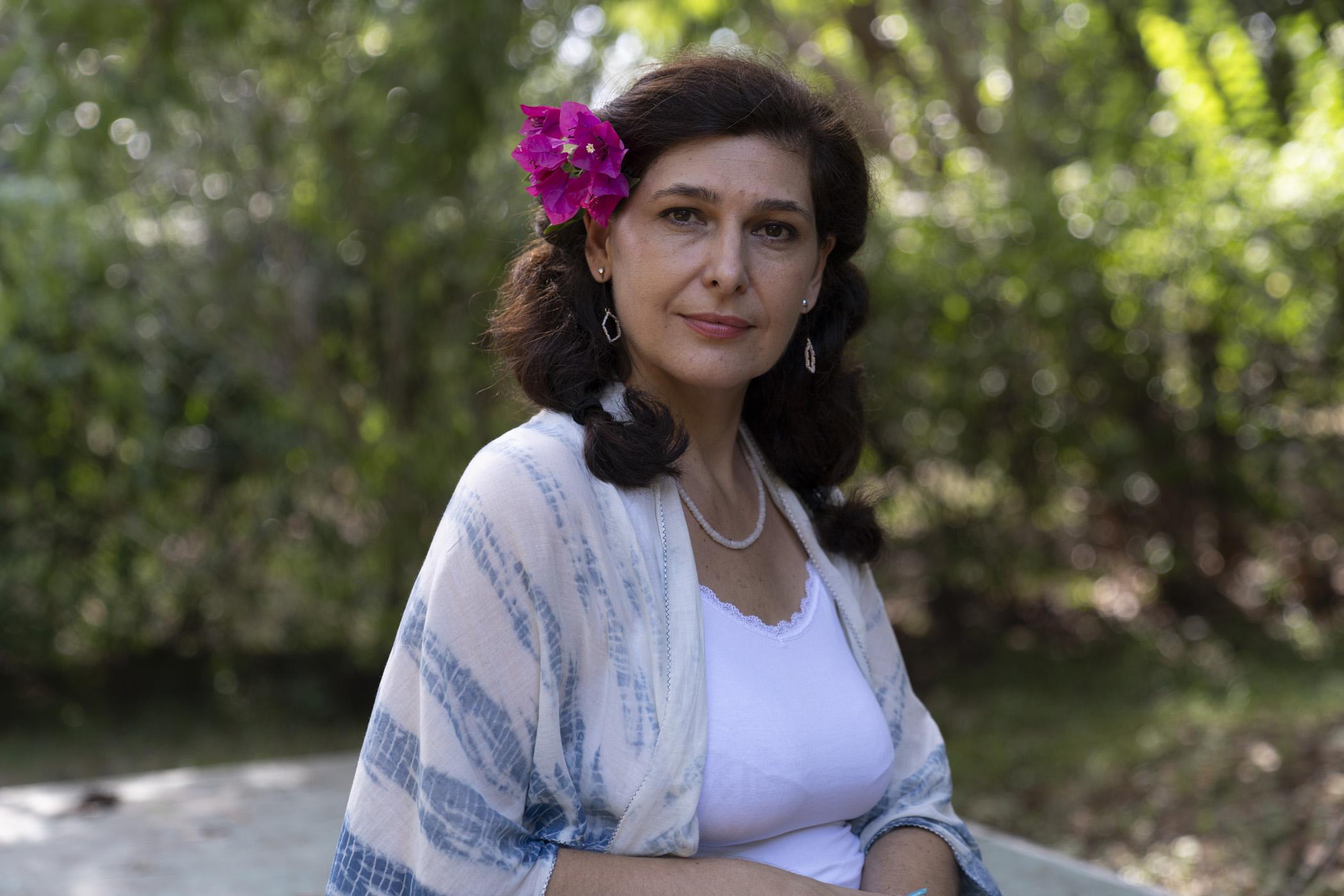 A woman with brown hair and a purple flower in her hair stares at the camera.