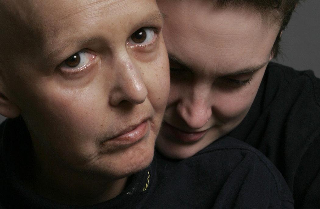 A closeup of two women leaning on each other. The woman in front looks into the camera.