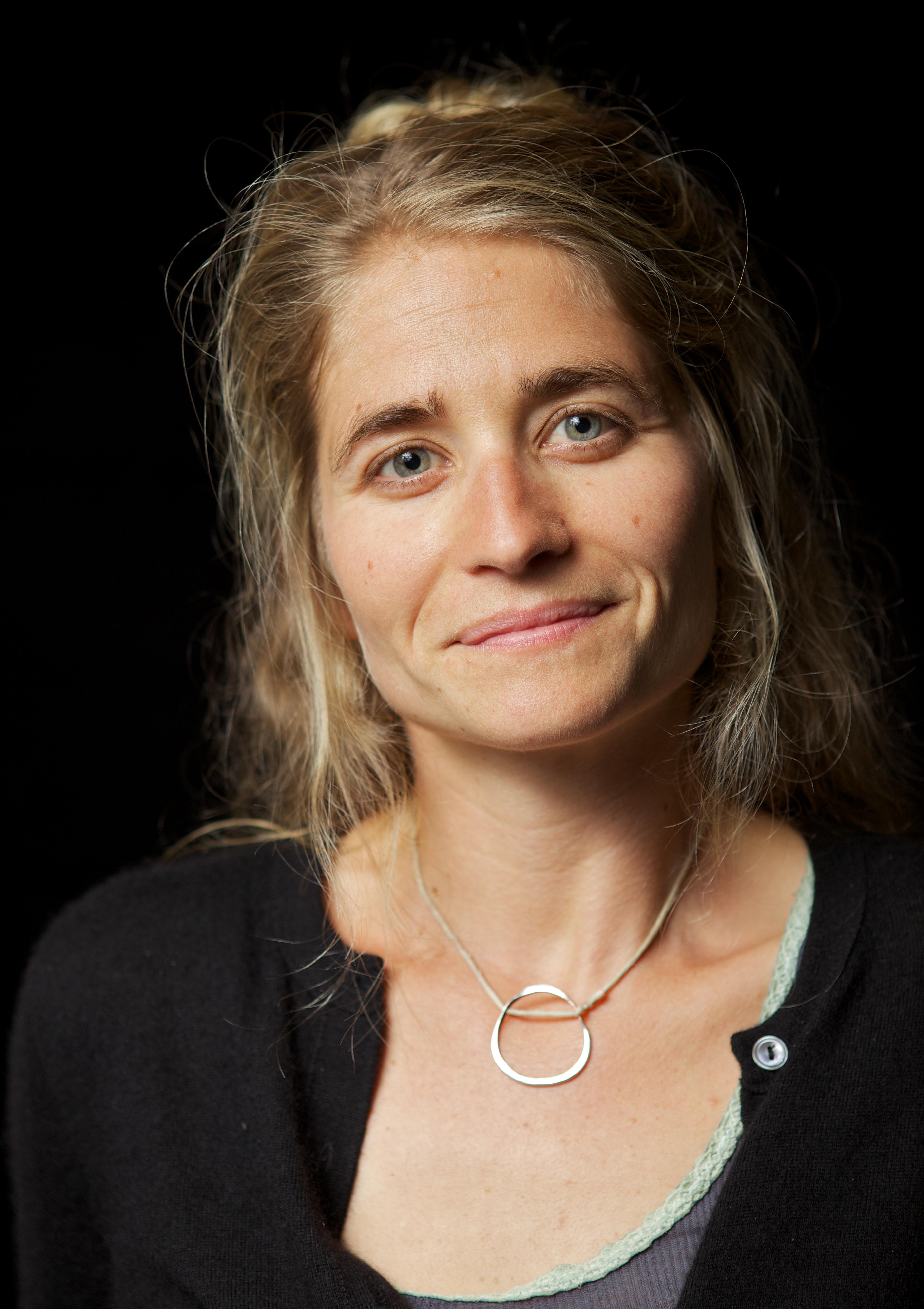 A portrait of a woman smiling into the camera in front of a black backdrop.