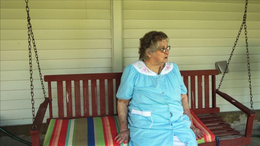 Still from Cheshire, Ohio. An elderly woman is sitting on a colorful bench.