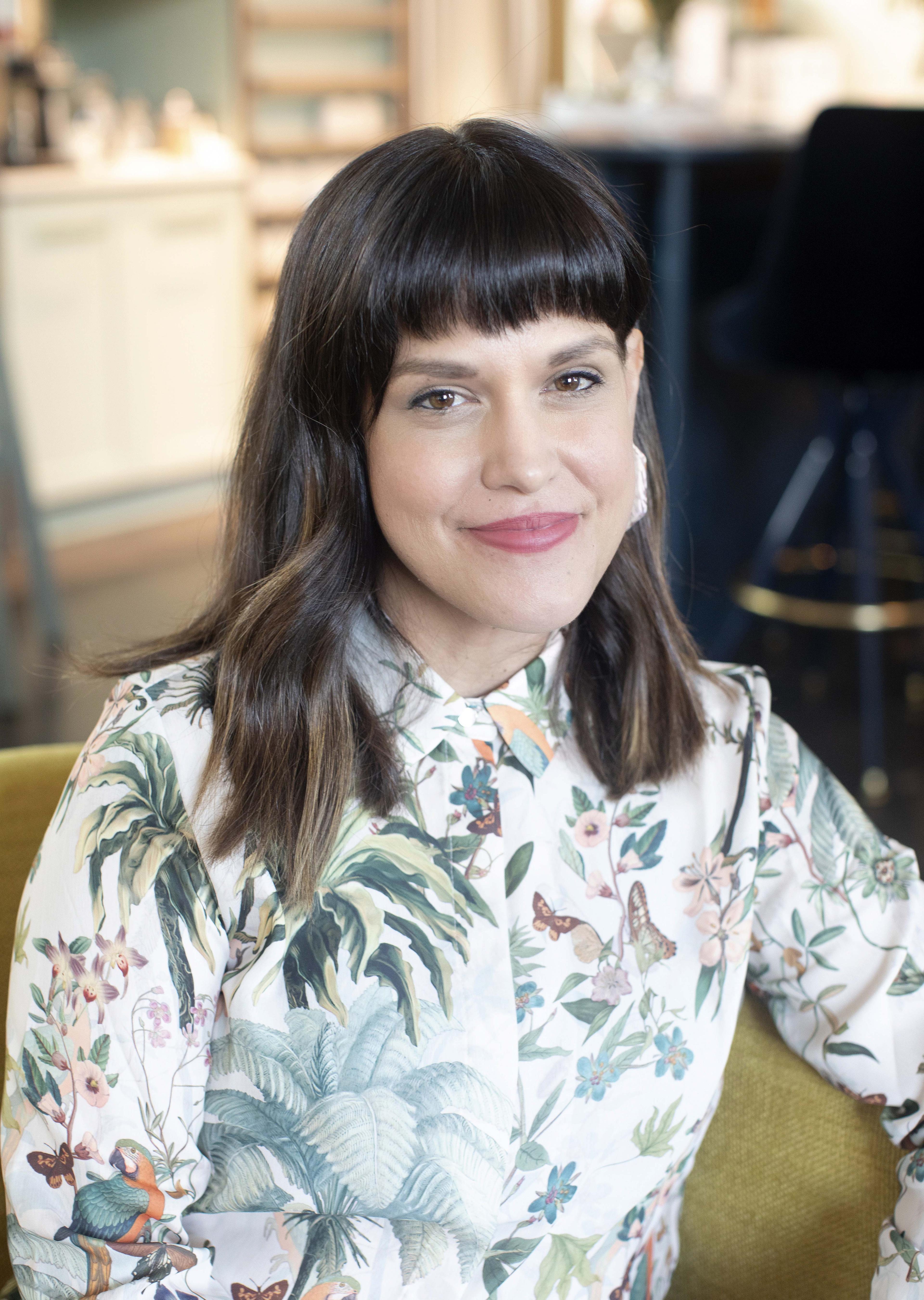 The Director of Matininó, Gabriela Diaz Arp, wears a long-sleeve, tropical print button down shirt and sits on a yellow chair to pose for a photo.