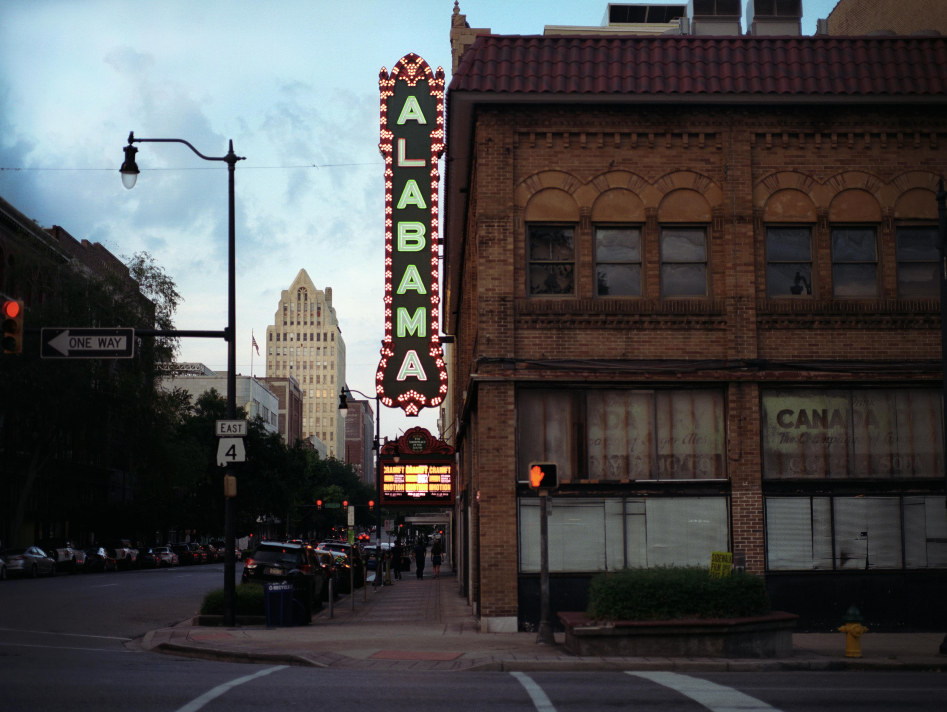 A photo of the Alabama Theater at dusk. A retro, neon sign reads "Alabama." In the distance, an old theater sign reads "craft in motion."